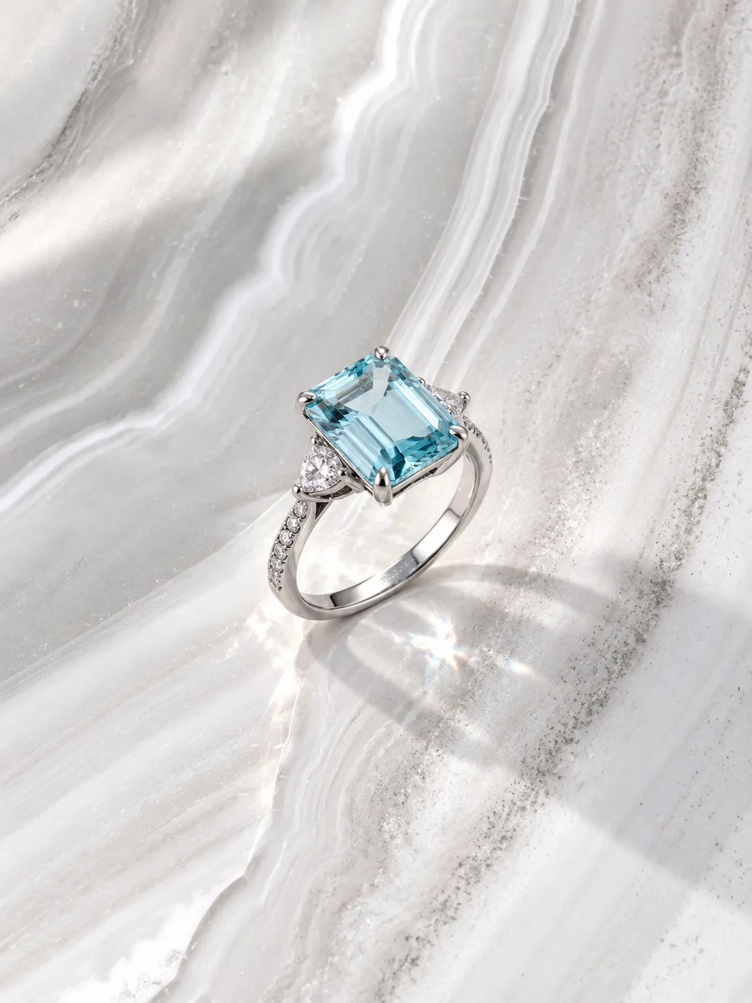 Emerald-cut aquamarine ring with diamond side stones on marble