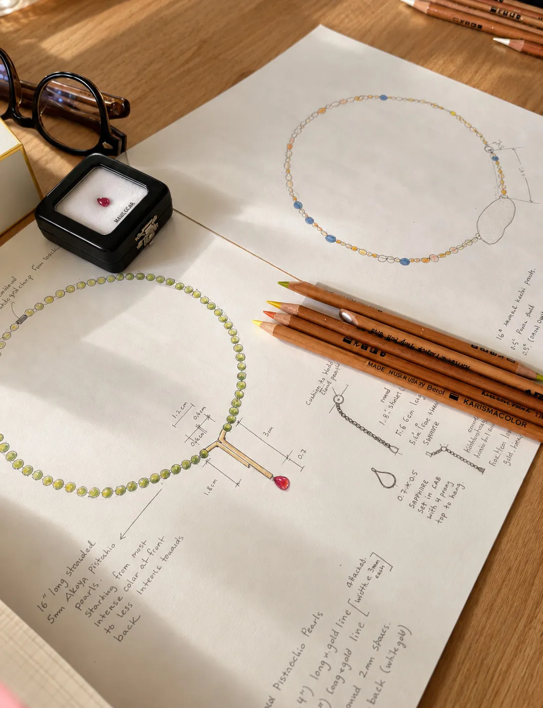Design desk with necklace sketches, coloured pencils and a loose gemstone