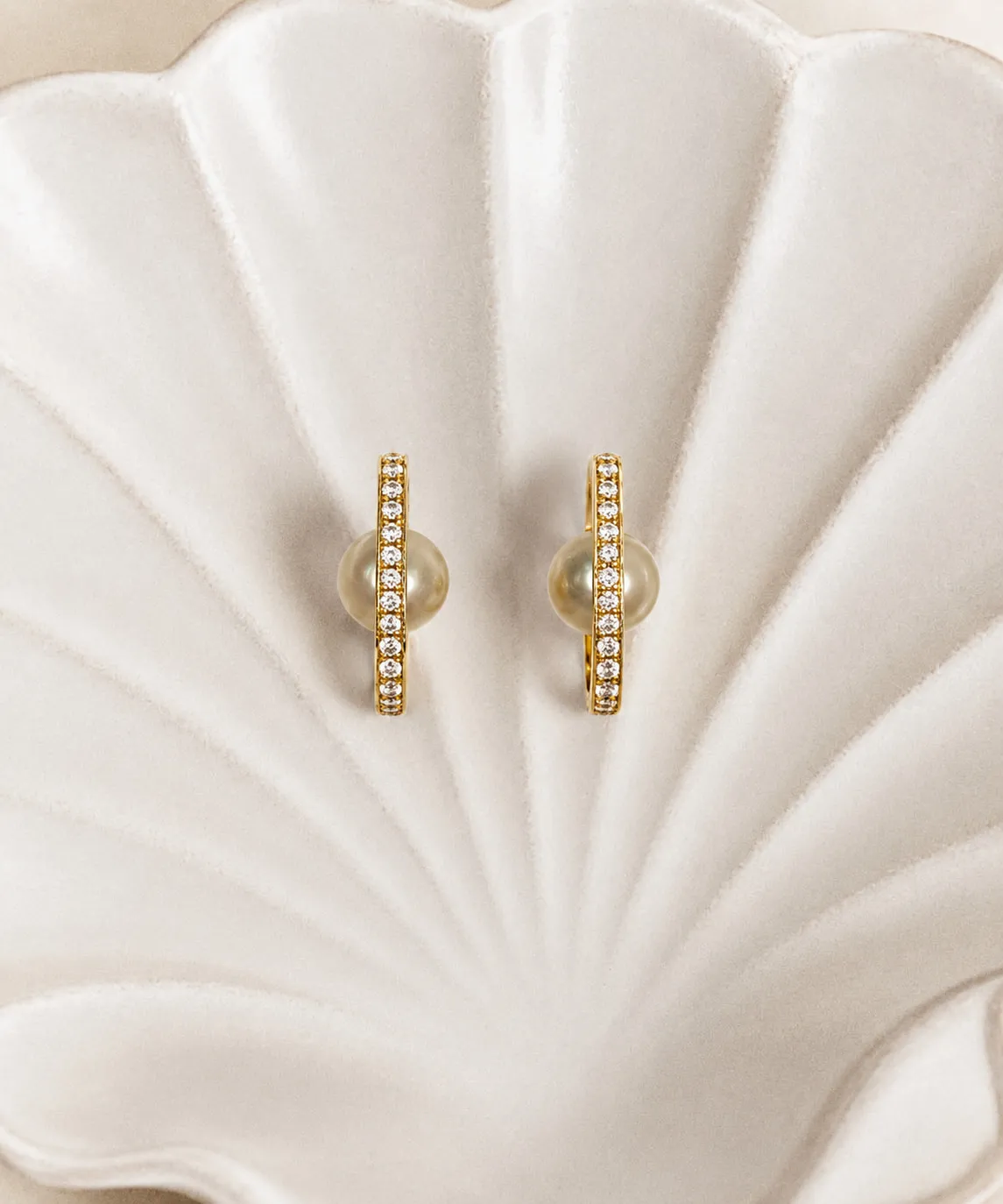 Gold and diamond hoop earrings with golden pearls, resting in a shell dish