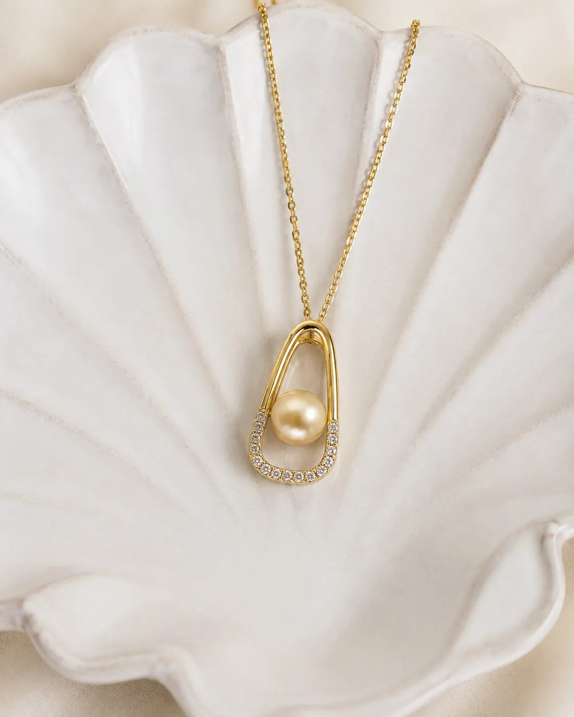 Golden pearl held in an open gold and diamond pendant, resting in a shell dish