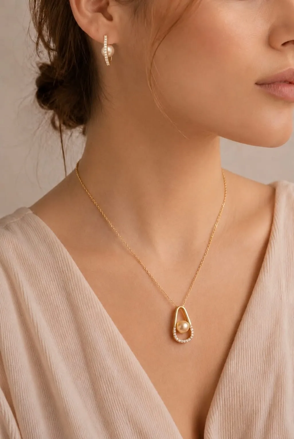 Golden pearl pendant worn with a blush neckline