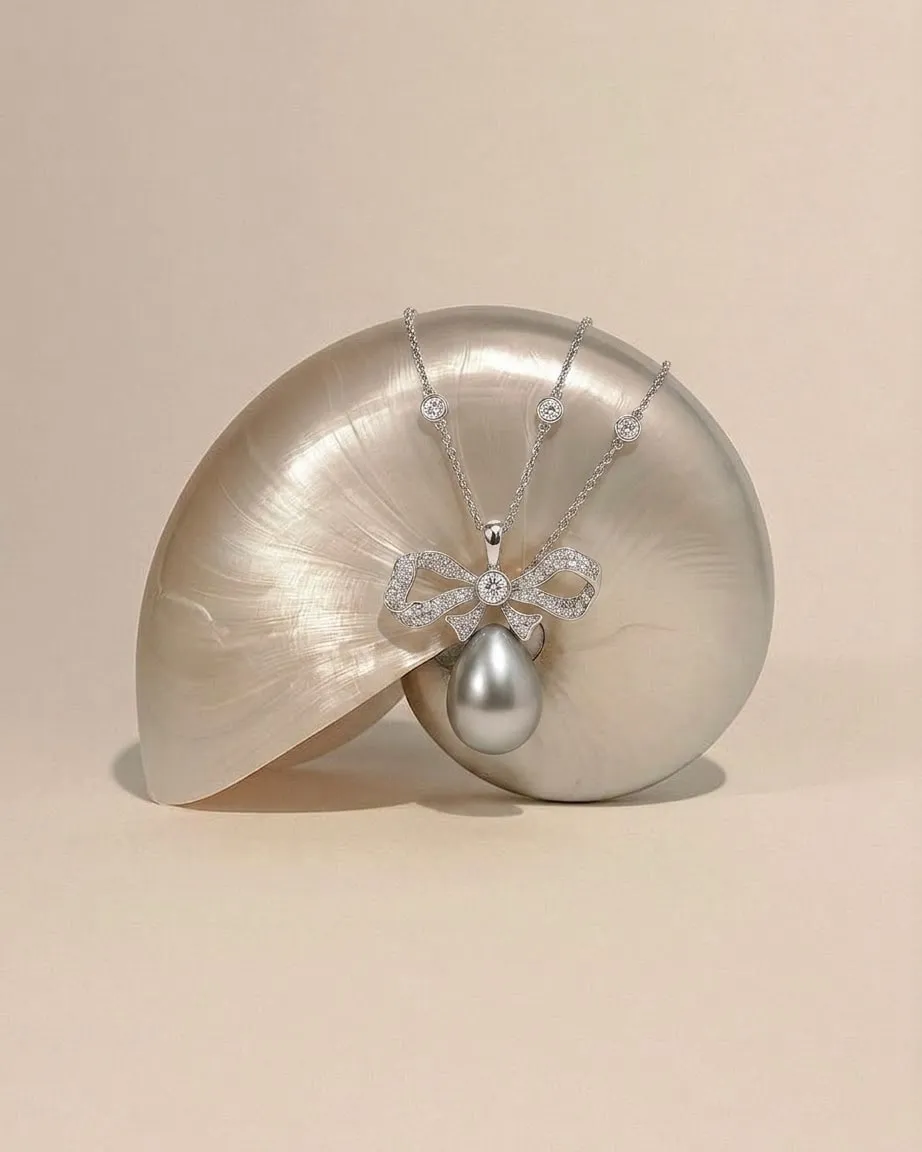 Diamond bow pendant with a grey pearl drop, draped over a nautilus shell