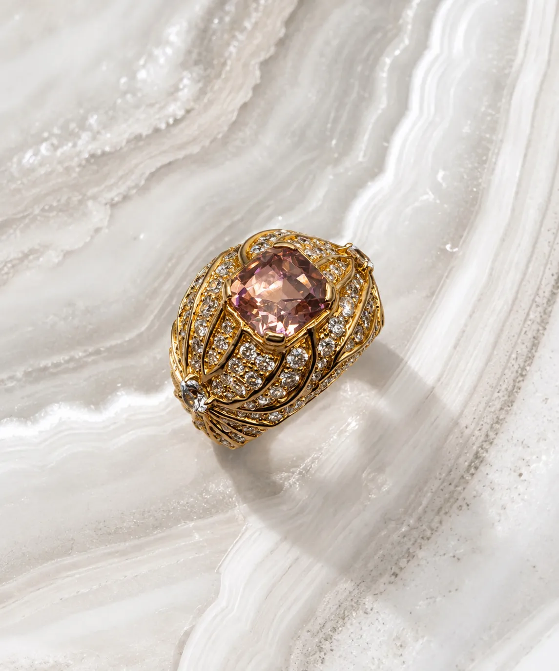 Gold and diamond cage ring with a pink gemstone centre on marble