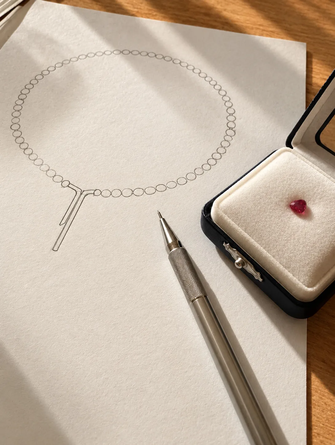 Pencil sketch of a necklace beside a loose red gemstone in a box